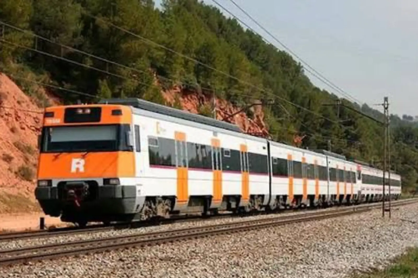Tren de cercanías blanco y naranja circulando por una vía férrea entre árboles y taludes de tierra